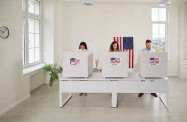 Kendine güvenen bir grup genç Amerikan vatandaşı oy verme merkezinde sırada bekliyor ve oy verme kabininde ABD bayrakları var. Seçim günü oy kullanma merkezindeki insanlar. Demokrasi kavramı.
