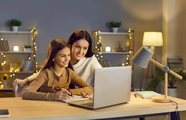 stock image Young cheerful happy mother with her teen school girl daughter studying online class on laptop at home during remote lesson. Woman parent helping child with homework. Distance education.