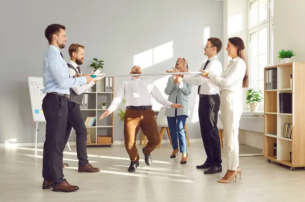 stock image Office workers, colleagues and coworkers, are playing the limbo game and dancing at an office party event. The atmosphere is festive as they celebrate together, showcasing team spirit and group fun.