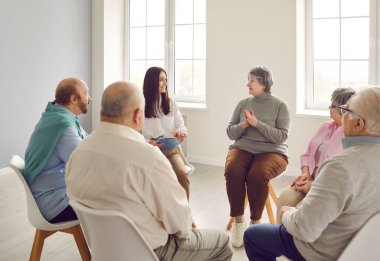 Grup terapi toplantısında kıdemli insanlar konuşuyor. Huzurevindeki yaşlı erkek ve kadın hastalar, eğitim seminerindeki yaşlanma sorunlarını not panosu olan genç, gülümseyen terapist kızla tartışıyor.