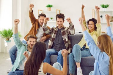 Bir grup arkadaş haftasonunu birlikte geçirip başarıyı kutluyor ve eğleniyorlar. Mutlu, neşeli, neşeli, evdeki kanepede ve yerde oturmuş gülümseyen ve ellerini kaldıran gençlerden oluşan bir takım.