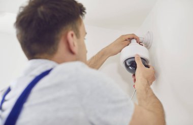 Beyaz erkek işçi ya da elektrikçi bir evin ya da ofisin duvarına güvenlik kamerası yerleştiriyor. Bu güvenlik sistemi iş yerinde ya da yaşam ortamında güvenliği, korumayı sağlar.