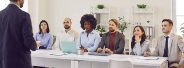 Şirketin müdürünün, ofiste dikilirken, çeşitli çalışanlarla bir atölye çalışması yaparken görüntüsü. İş stratejileri, iletişim ve takım çalışması için takım toplantısı