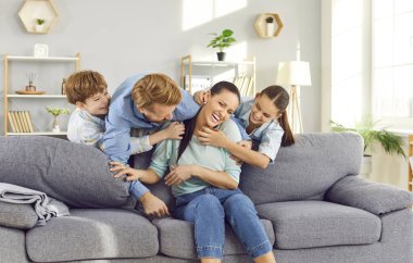 Mutlu, gülen çocukların portresi. Anne babalarıyla eğleniyorlar. Evdeki kanepede oturuyorlar. Çocuklarla vakit geçiren genç bir çiftin portresi. Aile eğlence konsepti.