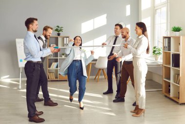 Eğlence, motivasyon ve iş birliği için eğlenceli ofis takımı etkinliği, limbo dansı yarışması. Düşük barın altında ileri doğru giden bir kadın, eğlenceli, eğlenceli, eğlenceli bir iş istirahatı, neşeli iş adamları