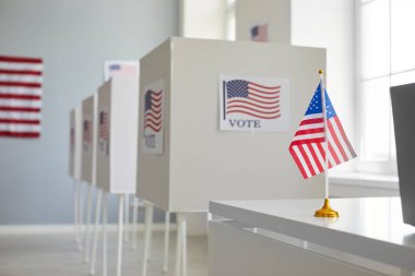 Oylama merkezinde Amerikan bayrağıyla süslenmiş sıra sıra beyaz oy kullanma kabinleri olan boş oy kullanma merkezi. Amerika Birleşik Devletleri 'nde başkanlık seçimleri. Demokrasi ve seçim günü konsepti.