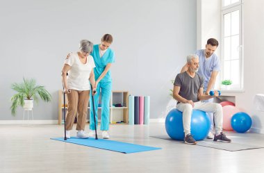 Rehabilitasyon kliniğinde spor yapan yetişkin insanlar ya da sağlık görevlilerinin yardımıyla egzersiz yapıyorlar. Fizyoterapistle beden eğitimi için egzersiz yapan emekli adam ve kadın.