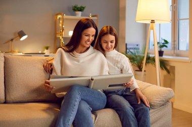 Gülümseyen anne ve kızı, akşamları oturma odasındaki kanepede oturup birlikte bir fotoğraf albümüne bakıyorlar. Anılardan ve anılardan bahsederek aile anlarından hoşlanırlar..