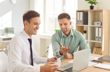 İş yerindeki işadamları. İki genç kendine güvenen çalışan toplantı masasında oturmuş dizüstü bilgisayar ekranına bakıyor yeni projeleri ya da girişimleri tartışıyor, şirketi analiz ediyor..