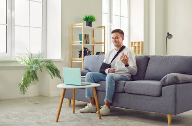 Kolu alçıda gülümseyen genç adam evdeki kanepede oturuyor ve dizüstü bilgisayarla iletişim kuruyor. Evde yaralandıktan sonra rehabilitasyonda olan bir adam bilgisayarda sohbet ediyor ve online video görüşmesi yapıyor..