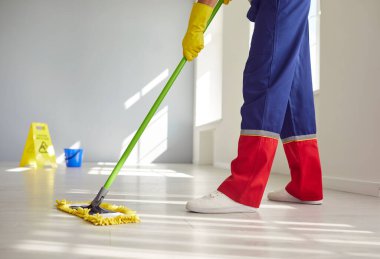 Temizlik şirketinin profesyonel temizlikçisi binada çalışıyor, yerleri paspaslıyor, kapalı alanı temiz ve hijyenik tutuyor. Hademe paspas tutuyor, düşük kesim çekim, iş kıyafetleri içinde bacaklar.