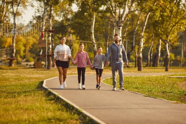 Spor kıyafetleri giymiş spor elbiseli mutlu bir aile spor antrenmanından sonra parkta el ele yürüyorlar. Doğa konseptinde sağlıklı yaşam tarzı, eğitim ve uygunluk.