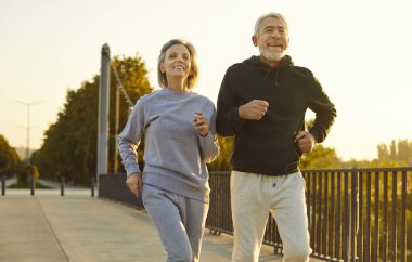 Mutlu gülümseyen son sınıf öğrencileri spor kıyafetleri giyip dışarıda koşuyorlar spor yapıyorlar. Dışarıda egzersiz yapan yaşlı çiftler ve kadınlar. Doğa koşusu ve sağlıklı yaşam tarzı konsepti.