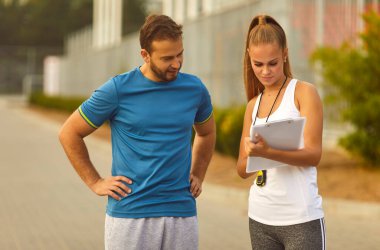 Spor eğitiminin sonuçlarını izleyen bir çift şehir parkında gösteri süresini kontrol ediyor. Erkek ve kadın, doğada spor koşusu yaptıktan sonra ayakta duruyor. Sağlıklı yaşam tarzı kavramı.