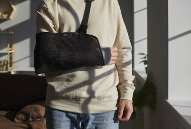 Evdeki ya da hastanedeki salonda yara üstüne rehabilitasyon gören alçılı bir adamın yakın plan fotoğrafı. Hasta askı ya da bandaj takıyor. İyileşme ve rehabilitasyon konsepti.