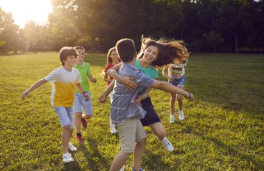Parkta kovalamaca oynayan mutlu çocuklar. Bir grup neşeli, heyecanlı çocuk yeşil çimlerde koşuyor, birbirlerini yakalamaya çalışıyorlar, güzel havanın tadını çıkarıyorlar ve birlikte harika vakit geçiriyorlar. Yaz tatili kavramı