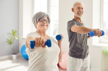 Spor kıyafetleri giyen erkek ve kadın sporcu kılıklı mutlu yaşlı insanların portresi spor salonunda birlikte egzersiz yapan halterlerle egzersiz yapıyorlar. Emeklilikte spor ve spor kavramı.