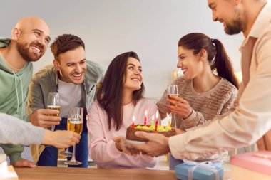 Gülümseyen genç insanlar ellerinde şampanya kadehleriyle mutlu kız arkadaşlarını tebrik ediyorlar doğum gününde masada oturuyorlar ve ona evde pasta veriyorlar. Doğum günü partisi ve kutlama konsepti.
