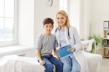 Dostane gülümseyen, doktor bir doktorun portresi randevu ile rapor tutuyor ve klinikteki tıbbi muayene sırasında çocuk bir hastaya sarılıyor..