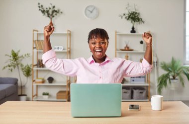 İş yerinde tişört giyen mutlu genç bir iş kadınının portresi. Başarılı bir anlaşmayı kutlayan ya da kontrat imzalayan biri gibi yumruklarıyla evet hareketi yapıyor..