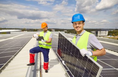 Güneş panellerinin montajı veya bakımı sırasında çatıda çalışan mutlu bir elektrikçinin portresi. Fotovoltaik sistem yenilenebilir enerji ve profesyonel uzmanlığı vurguluyor.