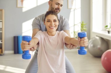 Spor salonunda kişisel eğitmen erkek hemşireyle rehabilitasyon seansı, dambıllarla spor egzersizi, rehberlik ve destekte yardımcı olan kişisel koç, bireysel eğitim programı.