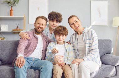 Evde gülümseyen mutlu bir aile, tasarruf bütçesi öğreten ebeveynler, gelecekteki alışverişleri birlikte planlayan küçük bir çocuk, küçük bir bankaya para koyan küçük bir çocuk, çocuklar için finansal eğitim, yatırım yapan bir çocuk.