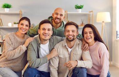 Memleketteki birkaç mutlu arkadaşın toplu portresi. Beş neşeli genç kanepede birlikte oturur, kameraya bakar ve güzel, beyaz dişlek gülümsemelerle gülümserler. Eğlence, arkadaşlık konsepti.