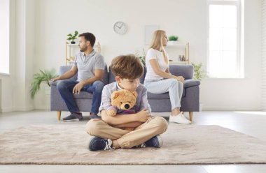 Hüsrana uğramış oğlu oyuncak ayıyla yerde otururken annesi ve babası evdeki tartışmalardan sonra kanepenin karşı tarafında oturup birbirlerini görmezden geliyorlar. Boşanma ve aile çatışmaları kavramı.