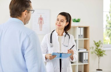 Olgun erkek hasta muayene sırasında klinikte duran gülümseyen bir bayanla konuşuyor. Hastaların şikayetlerini dinleyen bir tıp çalışanı. Sağlık hizmetleri kavramı.