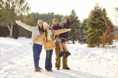 Mutlu gülümseyen dört çocuklu aile, iki kız ve erkek çocuk, kış parkında güzel doğanın tadını çıkarıyorlar. Genç ebeveynler ve çocukları karlı ormanda birlikte vakit geçirmenin keyfini çıkarıyorlar..