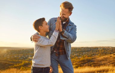 Mutlu baba ve oğul, tatilde ya da hafta sonu doğa üzerinde yürürken gülümseyerek beşlik çakar. Babalar gününde birlikteliğimizi, sevgimizi ve babalığımızı kutluyoruz..