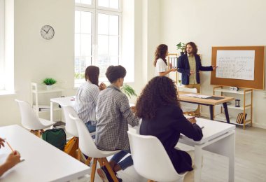 Sınıfta tahtada duran genç bir kız öğrenci ve bir ders sırasında üniversite veya lise öğrencilerinin önünde duran erkek öğretmene cevap veriyor. Eğitim ve öğrenme kavramı.