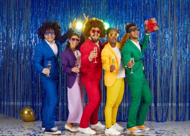 Full-size photo multinational funny group laughing happy cheerful people dressed in yellow, red, green suits, voluminous curly wigs and disco glasses with rhinestones on shiny festive blue background. clipart