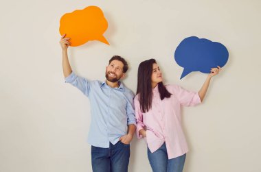 Stüdyo bej arka planda izole edilmiş kafalarının üstünde boş renkli konuşma baloncukları tutan kendine güvenen bir çiftin portresi. Düşüncelerinde kağıt bulutlar olan genç bir adam ve kadın.