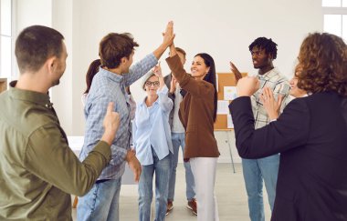 Başarılı olan çeşitli iş takımlarınız kutlu olsun. Bir grup neşeli, çok ırklı insan ofiste eğleniyor. Gülümseyen kadın erkek meslektaşına beşlik çakarken, diğerleri alkışlıyor ve alkışlıyor.