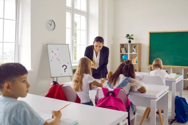 Parlak bir sınıfta bir grup ilkokul öğrencisi için ders veren pozitif kadın öğretmen. Öğrenciler öğretmen yardımı ile öğrenim ve öğrenim görmektedirler..