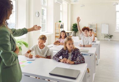 Okul öğretmeni ve mutlu öğrenciler sınıfta öğreniyor, öğrencilere soruyorlar. Bayan öğretmen, okul sırasındaki okul çocukları grubu, öğrenci çocuk el kaldırıyor, sınıfta soruları cevaplamaya hazır.