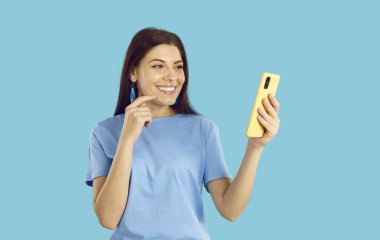 Gülümseyen genç beyaz kadın mavi stüdyo arka planında izole edilmiş cep telefonu interneti kullanıyor. Mutlu kız, akıllı telefon ekranındaki konuşmalara bak. Çevrimiçi iletişim.