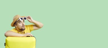 Vay canına, bu harika. Fotokopi uzay pankartında tatil valiziyle şaşırmış bir gezginin portresi. Açık yeşil telif alanı arka planındaki genç adam şaşkın mutlu yüz ifadesi olan bir şeye bakıyor.