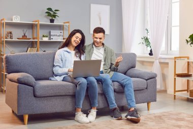 Çift kanepede dizüstü bilgisayarla oturup iyi haberi, başarıyı ya da zaferi kutluyor. Neşe ve kutlama, çevrimiçi bağlanma ve evin rahatlığında mutlu anın tadını çıkarma..