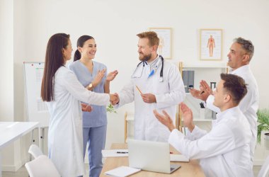 Mutlu gülümseyen doktorlar, klinikte ayakta kalarak tedavinin başarısına sevinerek el sıkışıyor. Hastanede beyaz üniformalı genç tıbbi personelden oluşan başarılı bir ekip. Sağlık hizmeti kavramı.