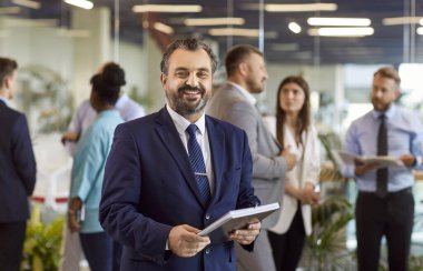 Kendine güvenen, olgun, ciddi iş adamı, başarılı şirket lideri, kurucu, profesyonel konuşmacı belgelerle poz veren, kameraya mutlu bakan, iş adamı portresi toplantıda