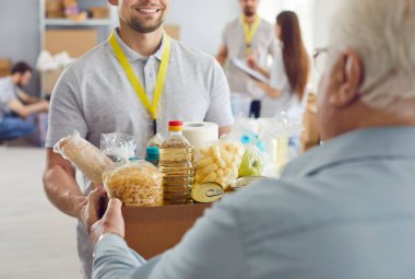 Gülümseyen gönüllü bir adam yaşlı bir adama bir kutu erzak veriyor. Yaşlılara bakım anlayışı, göçmenlere destek. Yeni yaşam koşullarına uyum sağlama, emeklilik yardımı, 