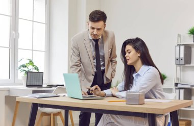 Ofiste gülümseyen iki şirket çalışanı. İş arkadaşları toplantı masasında oturmuş dizüstü bilgisayar ekranına bakıyor yeni projeleri veya girişimleri tartışıyor, şirketi analiz ediyorlar..