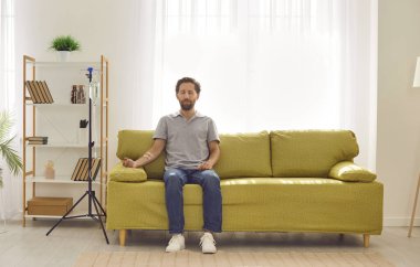 Evdeki ya da klinikteki kanepede oturan genç adam kanında serum ve vitamin tedavisi görürken. Günlük giysiler içinde üzgün bir erkek iğne terapisi görüyor..