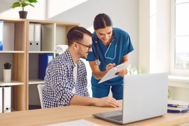 Kadın doktor, hastane ofisinde bir hastayla şefkatli bir konuşma yapar. Olumlu tıbbi iletişim, gülümsemelerle, hemşire sağlık sorunlarını tartışıyor ve tavsiyelerde bulunuyor.