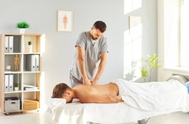 El terapisi seansı, fizyoterapistlerin vücut rahatlatıcı sırt masajı klinikte erkek hastaya masaj yapması, tıbbi kanepede yatması, osteopatik pratisyen, refleksoloji gerilim kaslarını gevşetmesi.