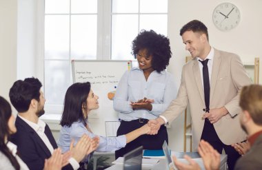 İş adamları toplantısı temsili, çeşitli işçiler yeni çalışanı destekliyor, masa başında el çırpma, terfi, başarılı takım arkadaşı desteği, kariyer gelişimi, profesyonel başarı.