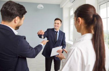 Profesyonel gülen emlakçı, emlakçı yeni ev sahiplerine evin anahtarlarını veriyor. Genç evli çift yeni bir ev ya da daire alıyor ya da kiralıyor. Gayrimenkul, mülk alımı.